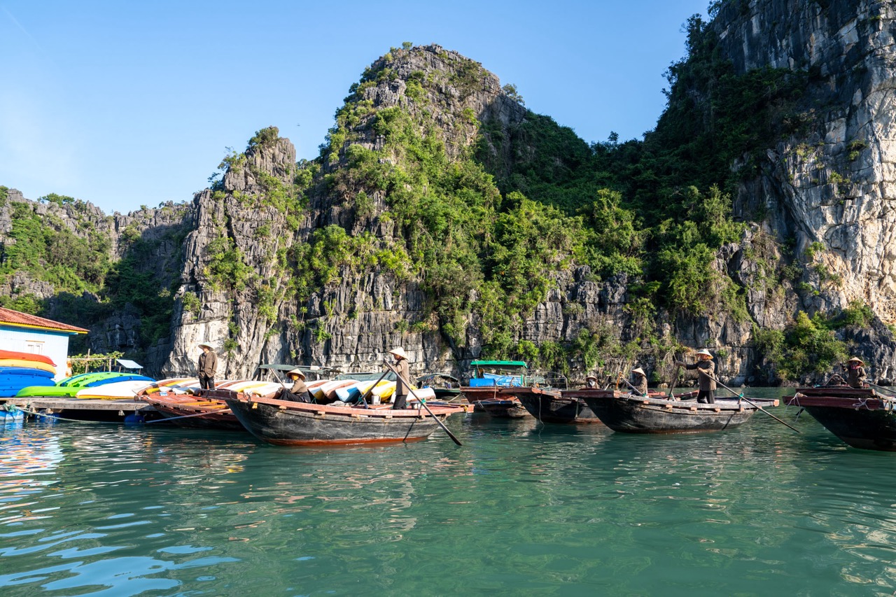 Scenic view of boats anchored near towering limestone cliffs in Bai Tu Long Bay during daytime.
