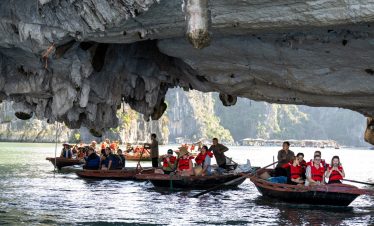 People kayaking under a large limestone cave in Bai Tu Long Bay, scenic and adventurous travel exper.