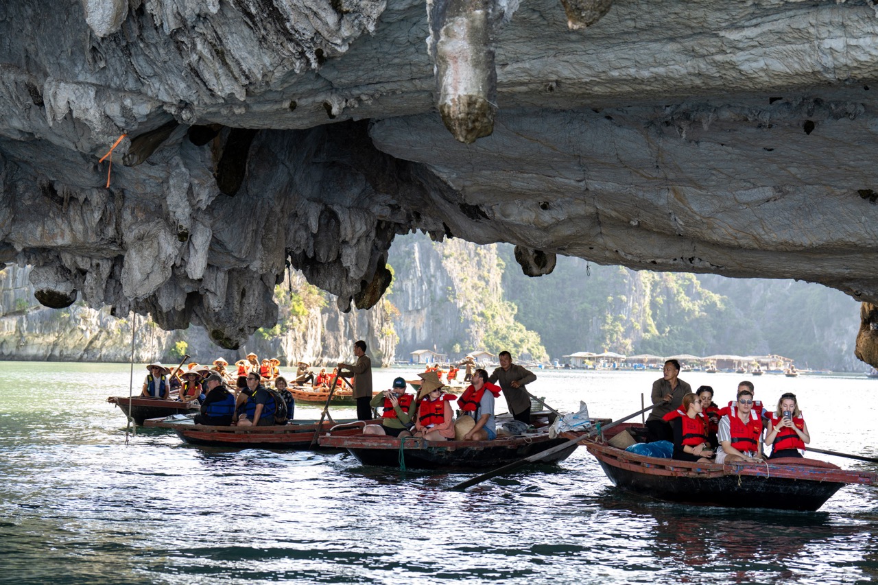 People kayaking under a large limestone cave in Bai Tu Long Bay, scenic and adventurous travel exper.