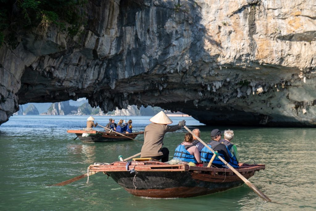 Scenic Bai Tu Long Bay cruise with people kayaking under dramatic limestone cliffs.