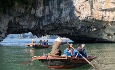 Scenic Bai Tu Long Bay cruise with people kayaking under dramatic limestone cliffs.