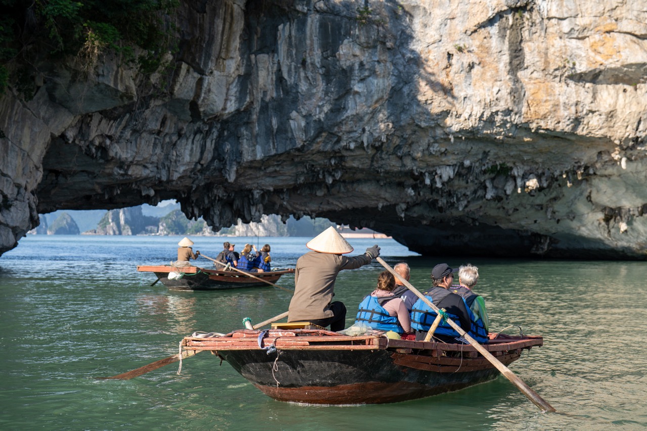 Scenic Bai Tu Long Bay cruise with people kayaking under dramatic limestone cliffs.