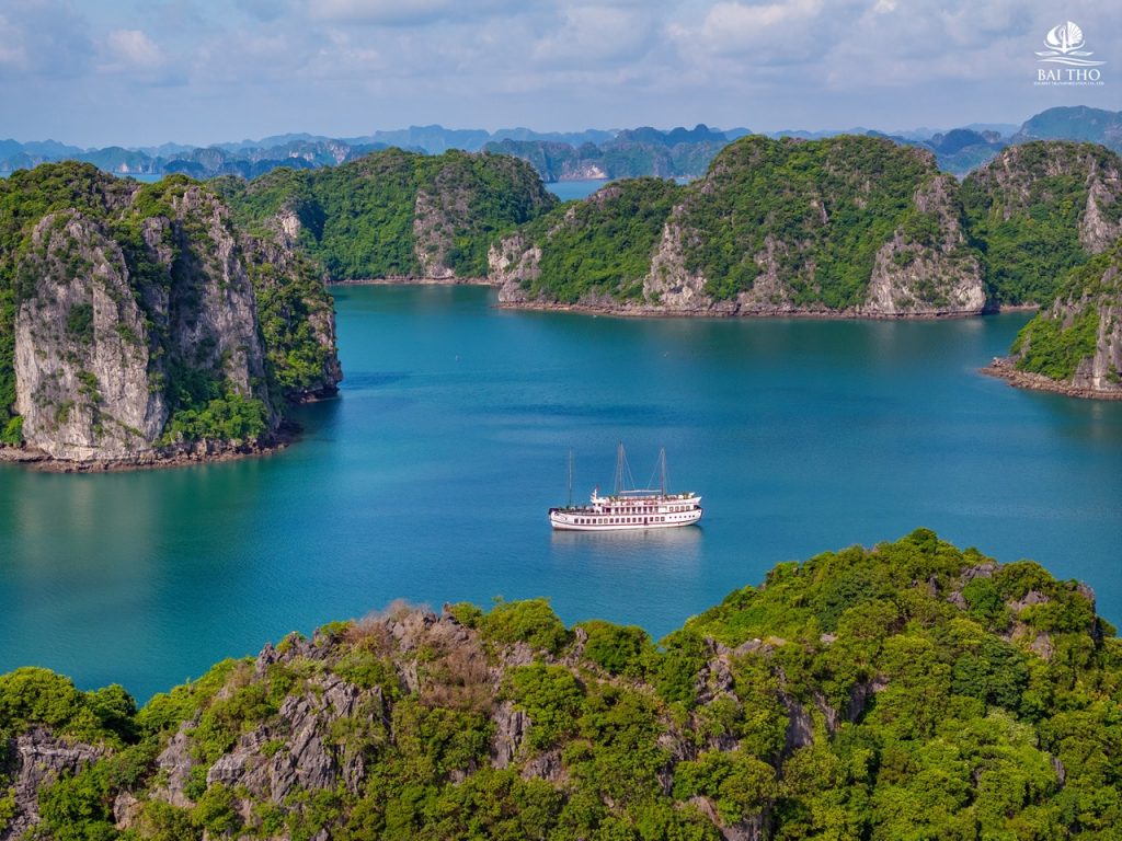 Scenic view of Bai Tu Long Bay with lush green islands and a cruise boat on tranquil waters, perfect.