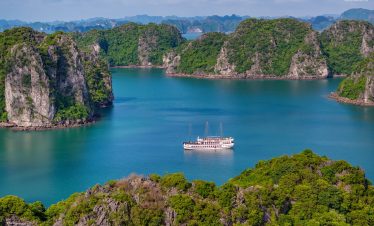 Scenic view of Bai Tu Long Bay with lush green islands and a cruise boat on tranquil waters, perfect.