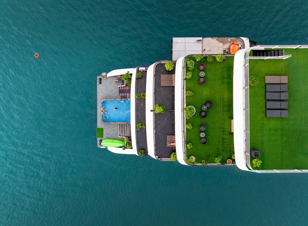 Aerial view of a luxury cruise ship with a pool and green deck, sailing in Lan Ha Bay, Vietnam.
