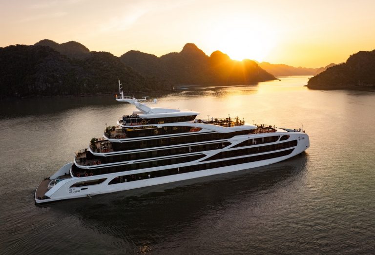 A modern luxury cruise ship sailing through Lan Ha Bay's stunning limestone karsts during sunset, pe.