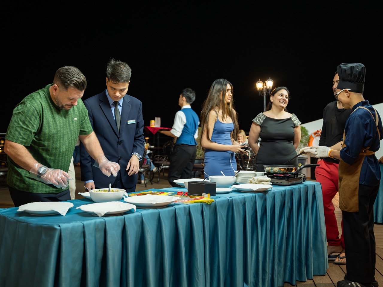 Guests enjoying a luxurious dinner on a cruise balcony in Lan Ha Bay at night.