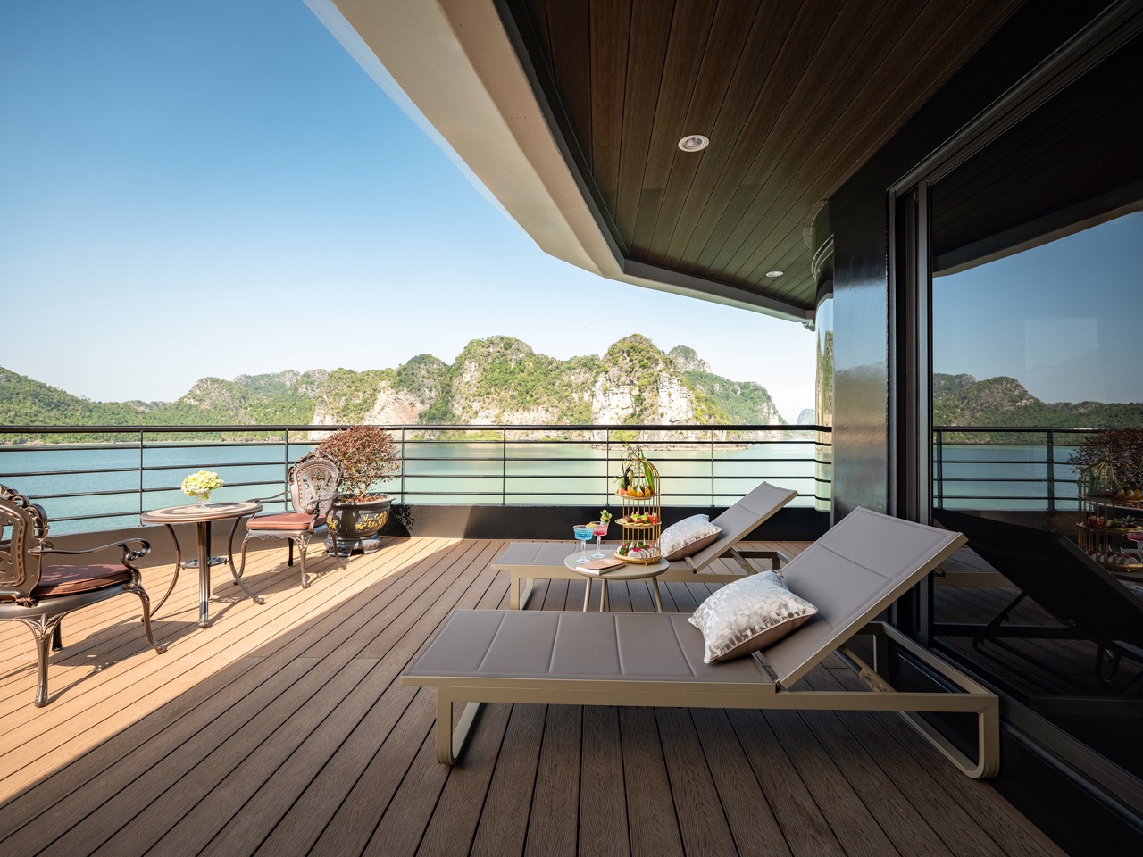 Stunning view from a luxury cruise balcony in Halong Bay with relaxing lounge chairs and scenic lime.