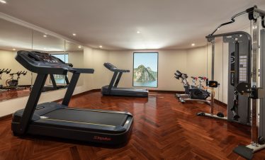 Bright and modern gym room on Lan Ha Bay cruise with treadmill, exercise bike, and scenic window vie.