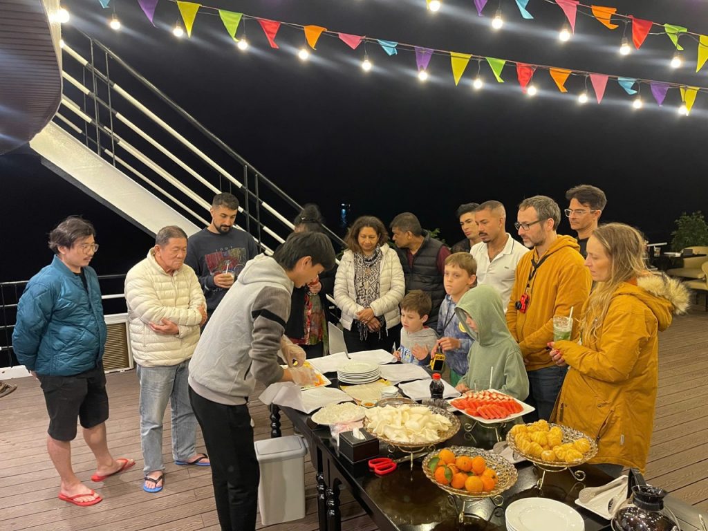 People enjoying dinner on cruise balcony at night in Halong Bay, festive atmosphere, vibrant lights,.