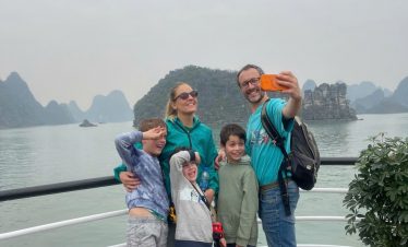 Happy family taking selfie on cruise balcony with stunning Halong Bay scenery and limestone islands.