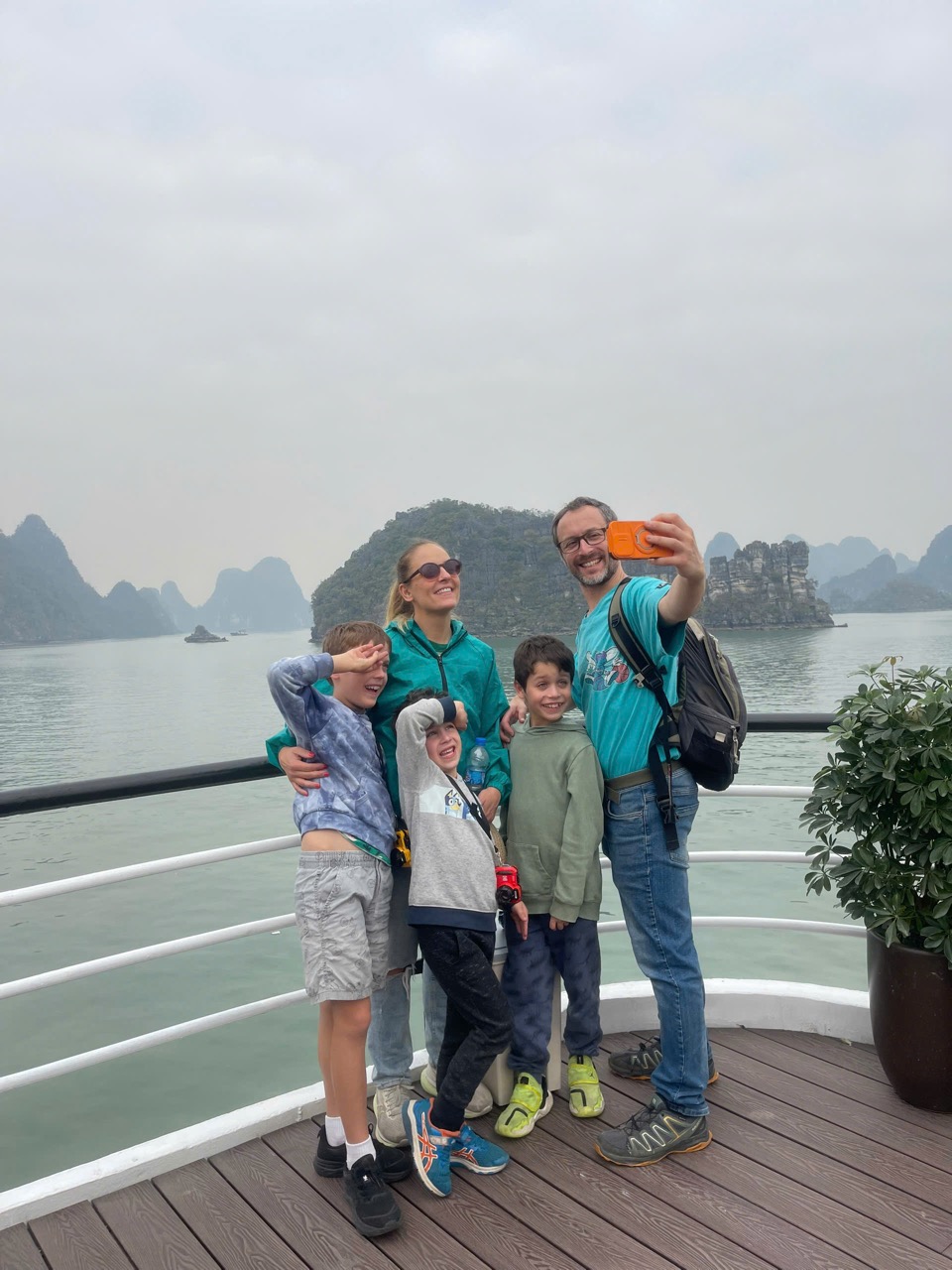Happy family taking selfie on cruise balcony with stunning Halong Bay scenery and limestone islands.