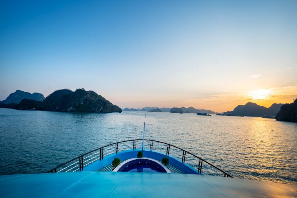 Lan Ha Bay cruise balcony with sunset view, scenic limestone islands, tranquil sea, and vibrant sky.