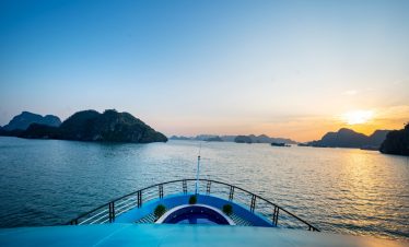 Lan Ha Bay cruise balcony with sunset view, scenic limestone islands, tranquil sea, and vibrant sky.