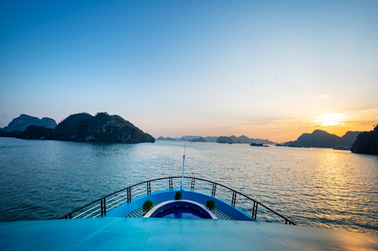 Lan Ha Bay cruise balcony with sunset view, scenic limestone islands, tranquil sea, and vibrant sky.