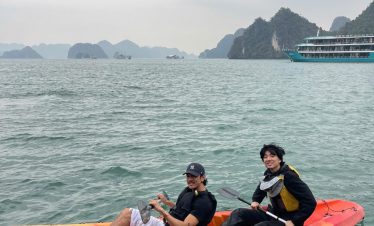 Two travelers kayaking on Lan Ha Bay with limestone islands and cloudy sky in the background.