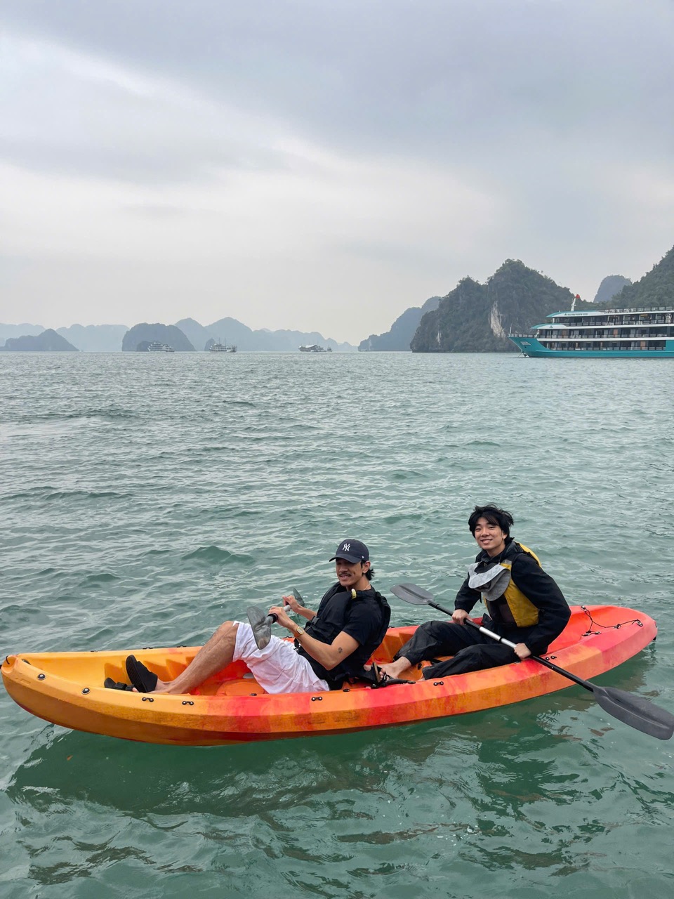 Two travelers kayaking on Lan Ha Bay with limestone islands and cloudy sky in the background.