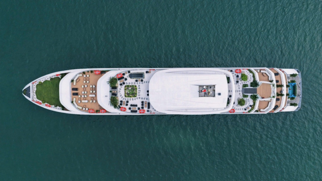 Aerial view of a large white luxury yacht cruising on calm blue water, seen from above.