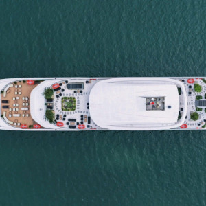 Aerial view of a large white luxury yacht cruising on calm blue water, seen from above.