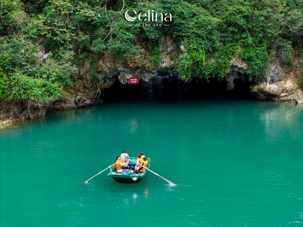 Boat with passengers in orange life jackets approaching a dark sea cave along turquoise water; lush green cliffs surround the scene; Celina of the sea logo visible above.