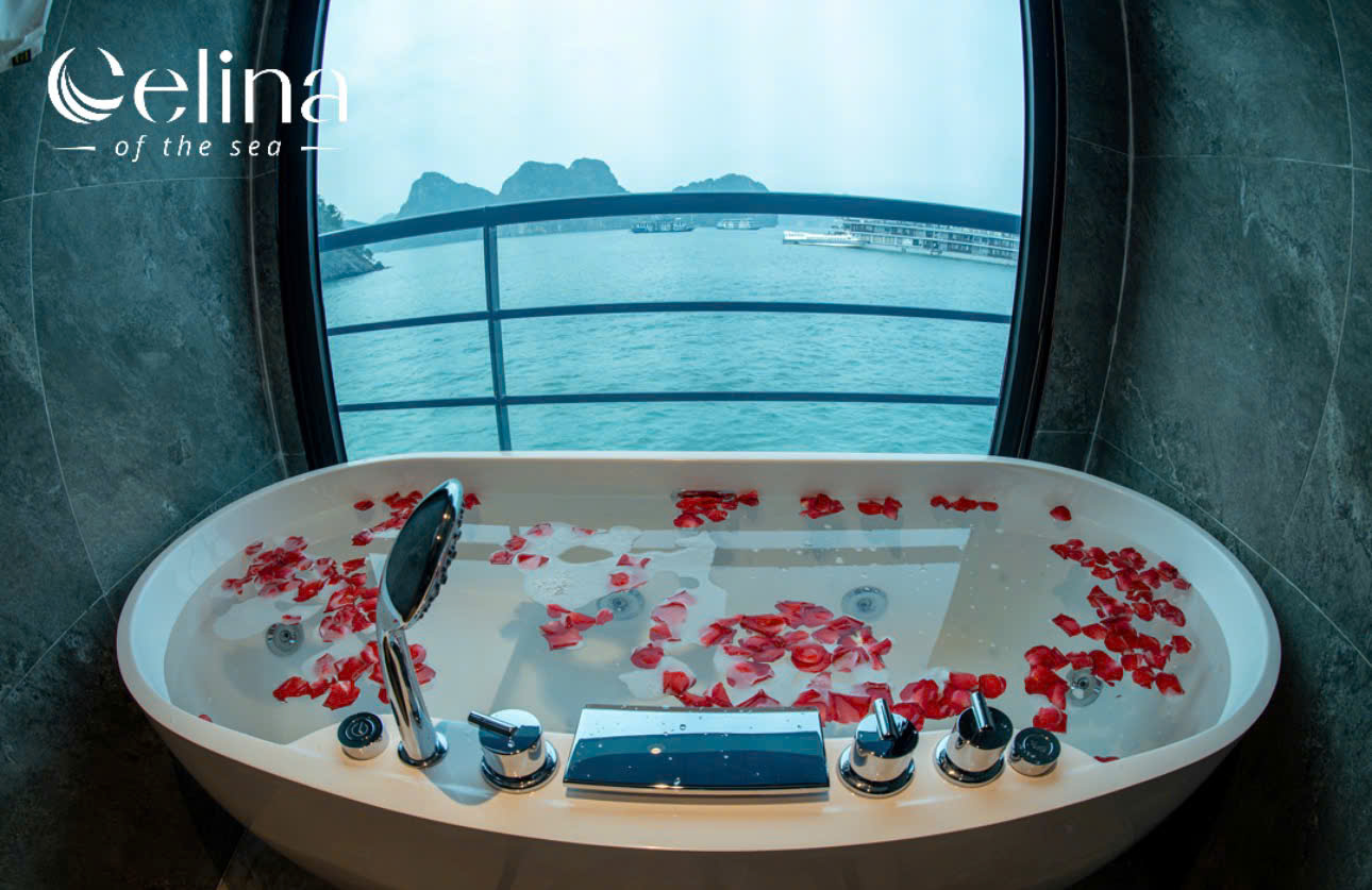 Luxurious white bathtub filled with water and red rose petals, ocean view through a curved window; Celina logo in the top-left corner.