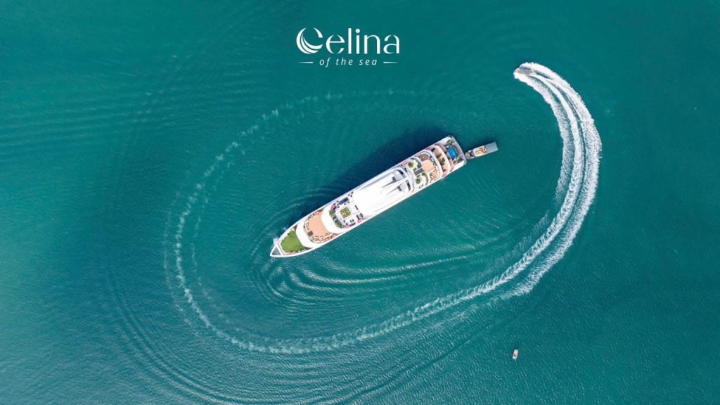 Aerial view of a white luxury yacht making a curved wake in clear turquoise water; Celina of the Sea logo at top.