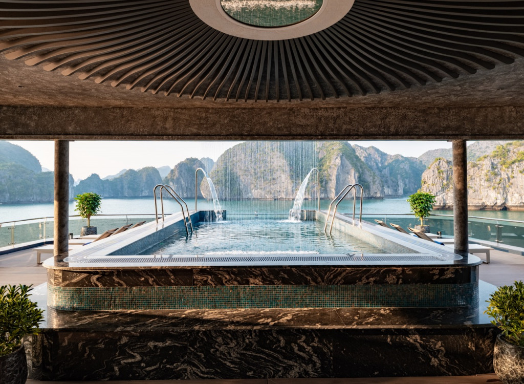 Luxurious indoor-outdoor pool framed by dark marble, with water jets and a bay of limestone karst rocks in the distance.