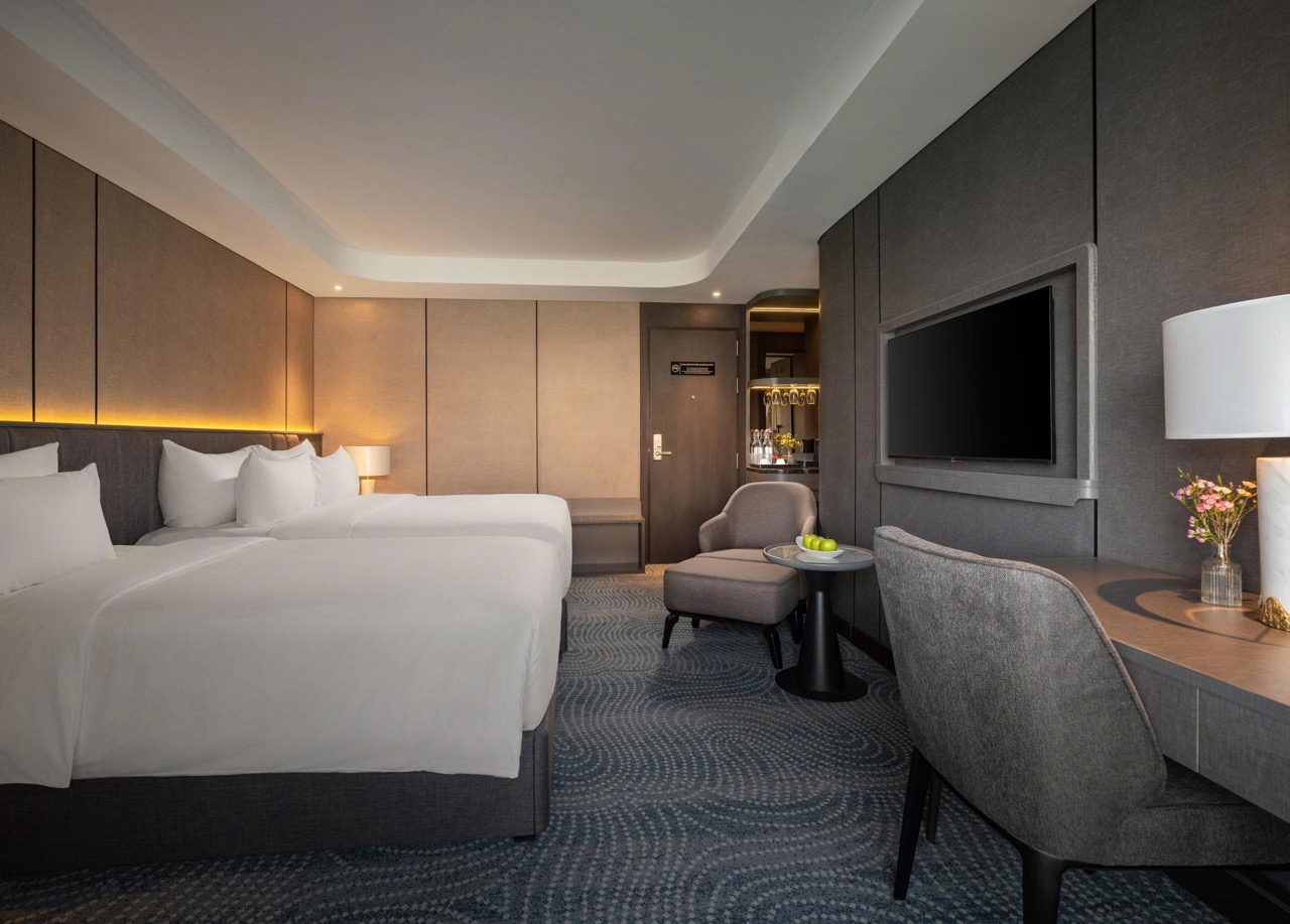 Two white beds in a modern hotel room with soft ambient lighting and a seating area nearby.