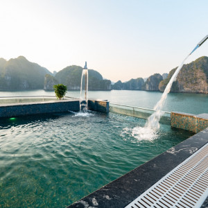 Resort pool overlooking turquoise water and limestone cliffs, with a curved fountain and water spilling into the pool at sunset.