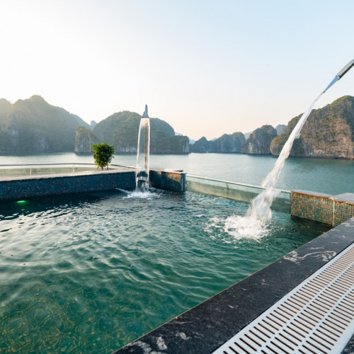 Resort pool overlooking turquoise water and limestone cliffs, with a curved fountain and water spilling into the pool at sunset.