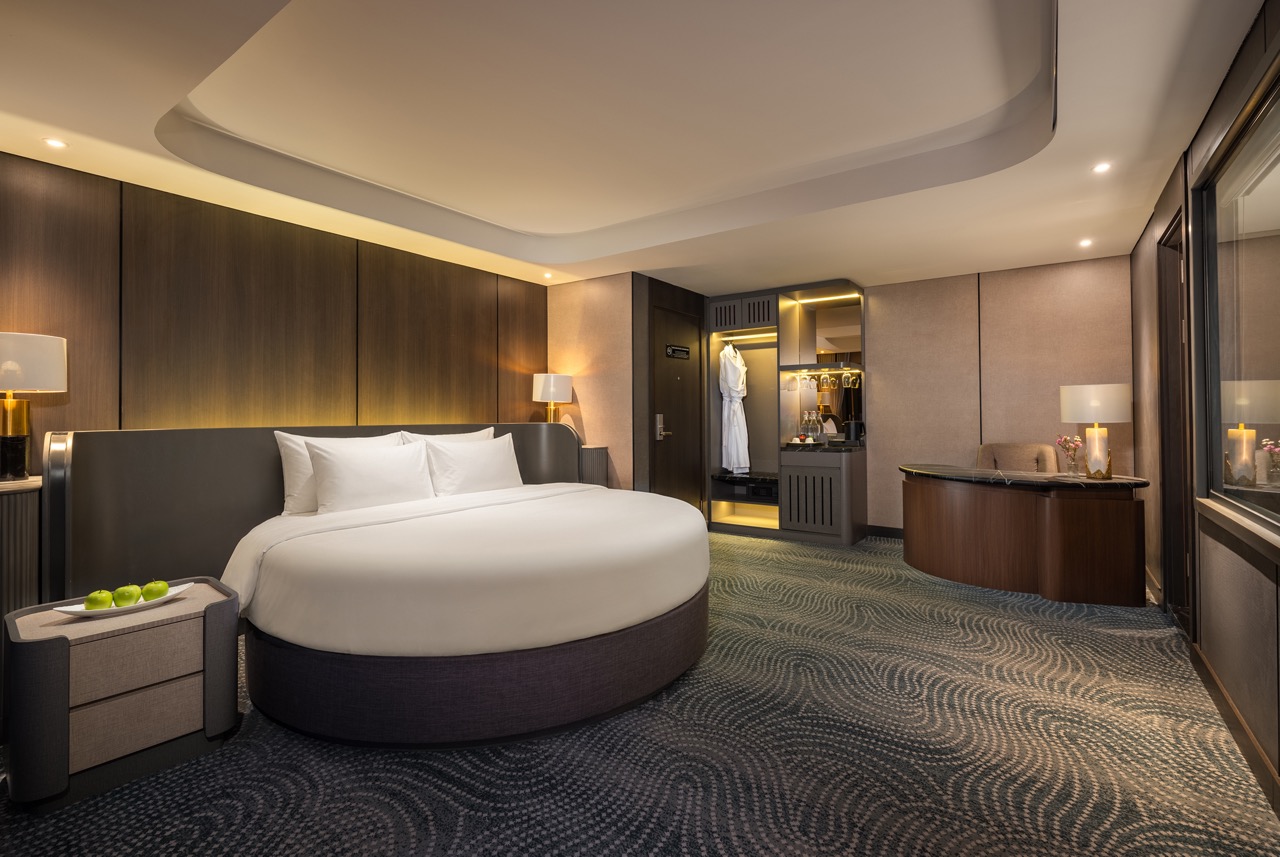 Luxurious hotel room with a circular bed, warm lighting, and an open closet containing a white bathrobe.