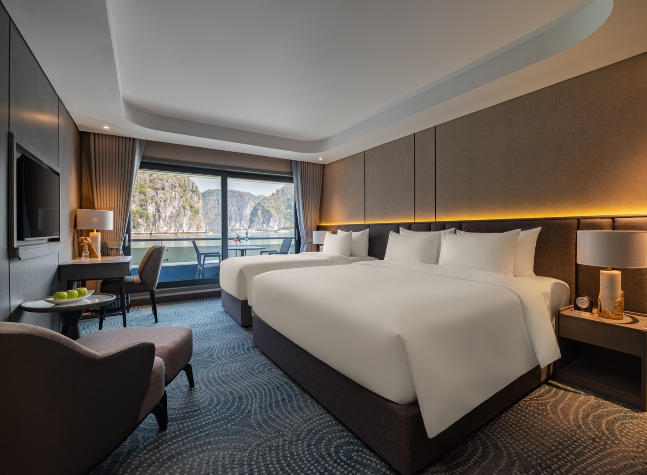 Hotel room with two large beds and a balcony view of rocky cliffs and water outside.