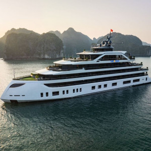 White luxury cruise yacht with multiple decks sailing in a calm bay at sunset, limestone cliffs in the background