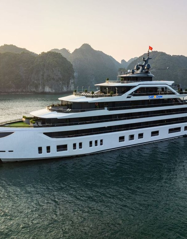 White luxury cruise yacht with multiple decks sailing in a calm bay at sunset, limestone cliffs in the background