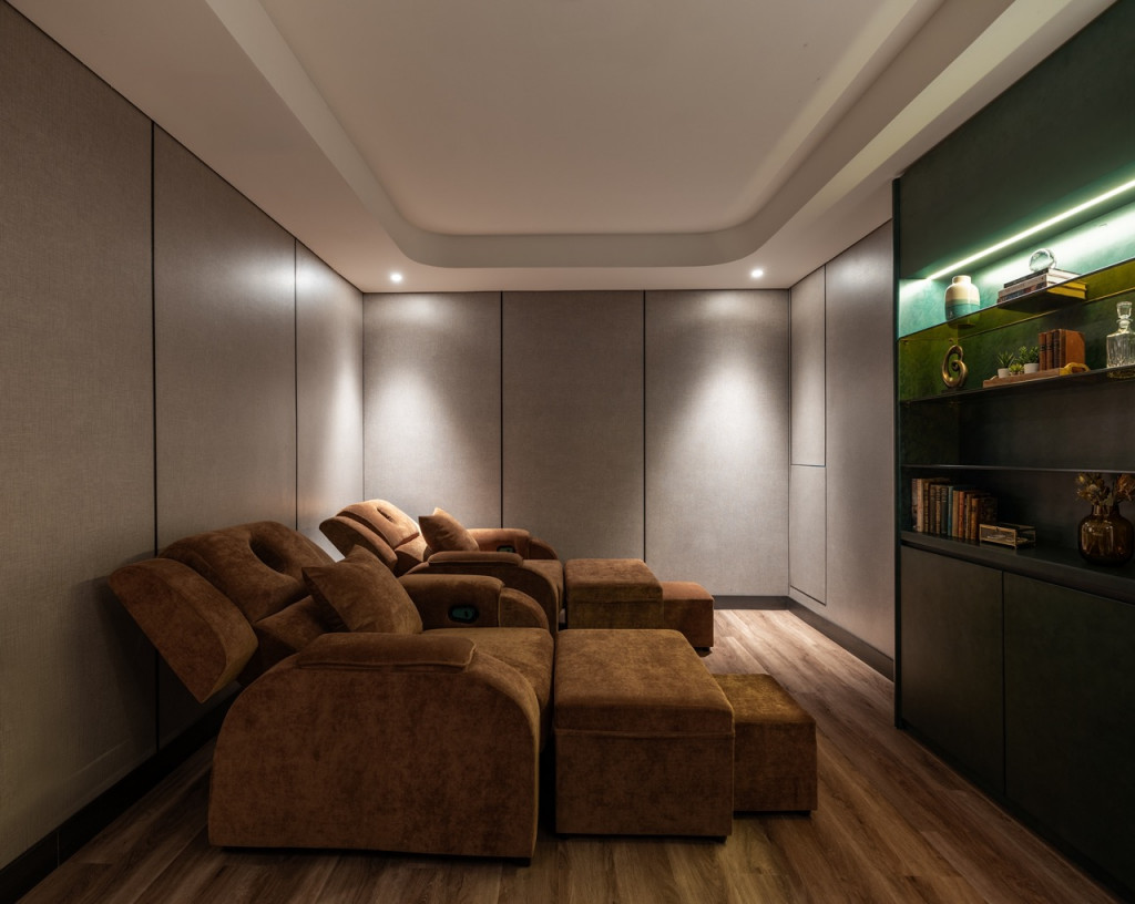 Cozy home theater lounge with plush brown sectional recliners and matching ottomans, dim ambient lighting, and wood flooring.