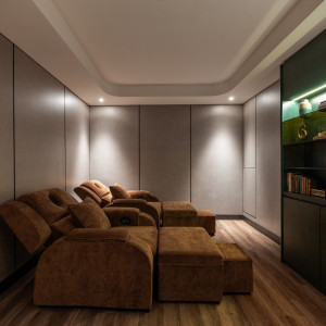Cozy home theater lounge with plush brown sectional recliners and matching ottomans, dim ambient lighting, and wood flooring.