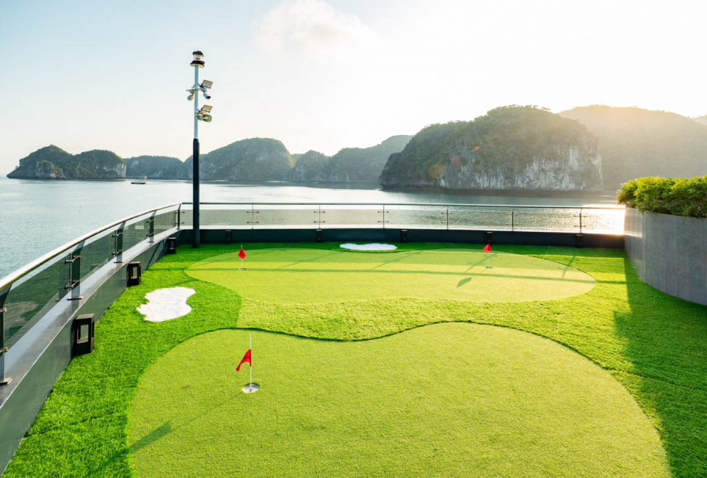 Rooftop mini-golf putting green by the seaside, with red flag holes and an ocean view.