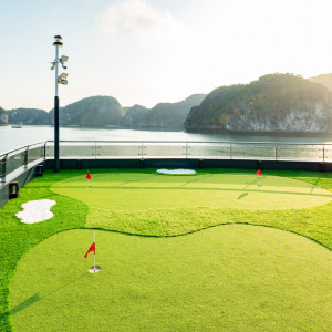 Rooftop mini-golf putting green by the seaside, with red flag holes and an ocean view.