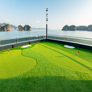 Miniature golf putting green on a ship deck with red-hole flags and a calm sea of rocky islets in the background