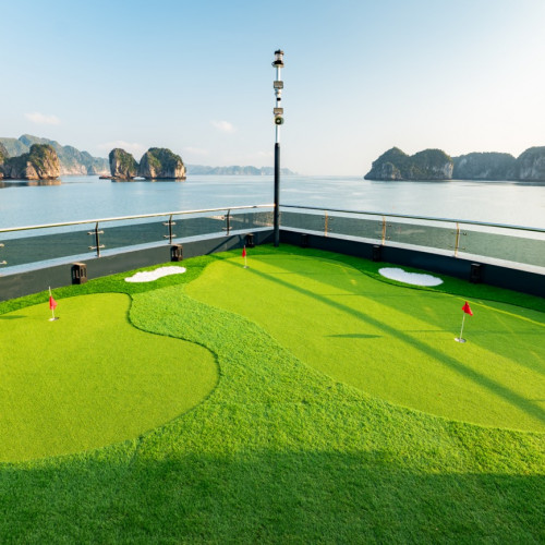 Miniature golf putting green on a ship deck with red-hole flags and a calm sea of rocky islets in the background