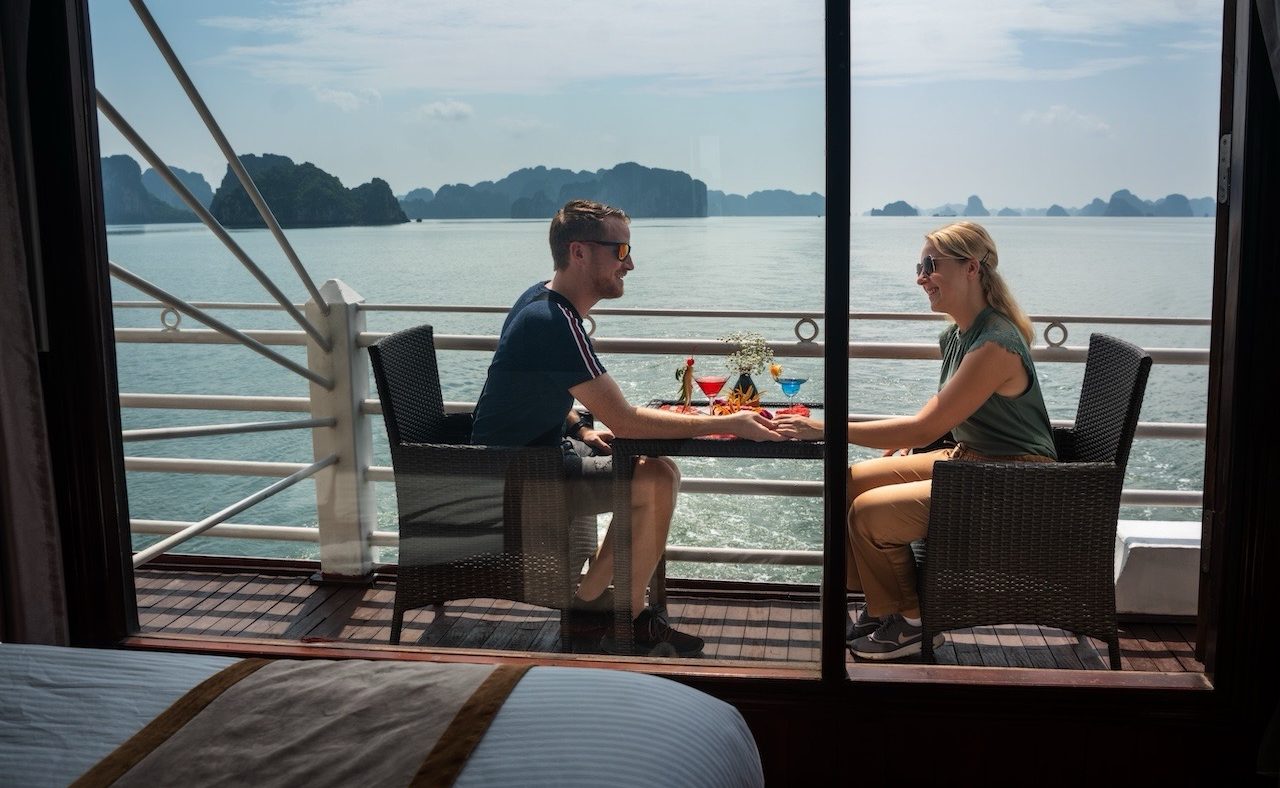 Couple enjoying dinner on a cruise balcony with stunning views of Halong Bay's limestone karsts and.